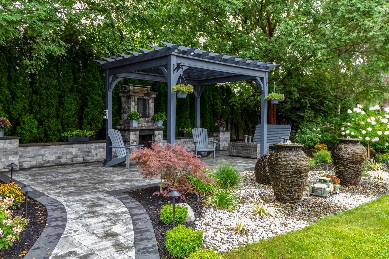 A beautiful backyard with a pergola, stone patio, and lush greenery.